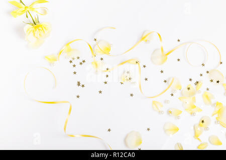 Beautiful bright yellow petals are flying on white background and a rose with ribbon, creative floral layout, horizontal. Overhead top view, flat lay. Stock Photo