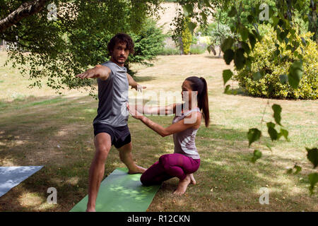 Female yoga teacher teaching young man yoga in garden, warrior pose Stock Photo