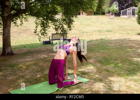 Woman practicing yoga in garden, bending over backwards Stock Photo