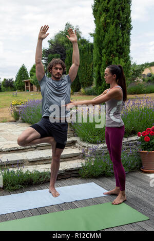 Female yoga teacher teaching young man yoga in garden, tree pose Stock Photo