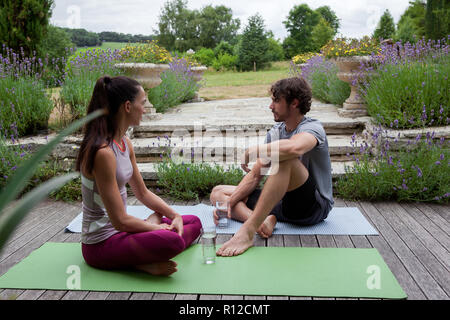 Man and woman practicing yoga in garden, taking a break on patio Stock Photo
