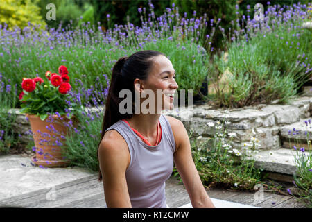 Woman practicing yoga in garden, taking a break on patio Stock Photo