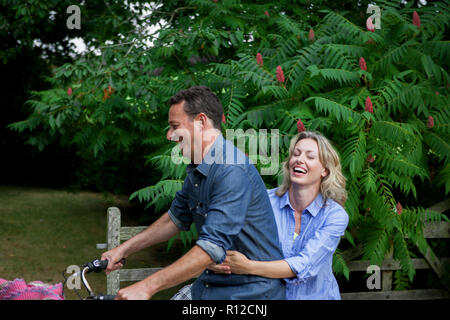 Mature woman riding pillion on bicycle on rural road Stock Photo