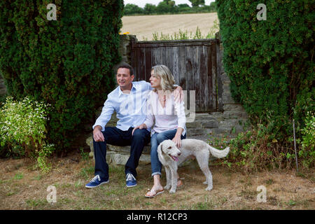 Romantic mature couple with dog sitting in garden Stock Photo