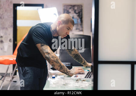 Tattooist using laptop in parlour Stock Photo