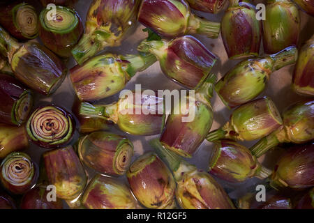 Prepared artichoke hearts floating in water for sale on a market stall Stock Photo