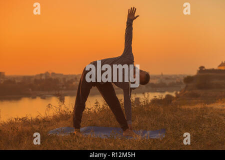 Man doing yoga on sunset with city view,Trikonasana /Triangle pose . Stock Photo