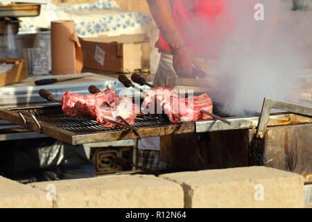 Appetizing delicious fried pieces of meat on skewers are roasted on a large grill in the open air. The chef prepares a barbecue. Stock Photo