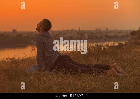 Man doing yoga on sunset with city view,Bhujangasana/Cobra Pose. Stock Photo