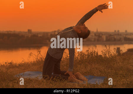 Man doing yoga on sunset with city view,variation of camel pose. Stock Photo
