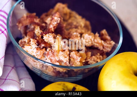 Apple crumble served in a small glass bowl with two apples aside Stock Photo