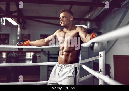 muscular professional kick boxer resting on the ropes in the corner of the ring while training for the next match Stock Photo