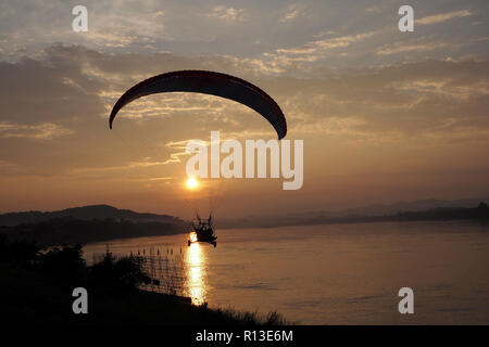 Silhouette of Paramotor flight over river with sunset Stock Photo