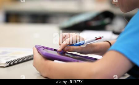 Student browsing the net using a purple tablet digital information technology tool devise to reseach during class time lesson at a modern high school  Stock Photo