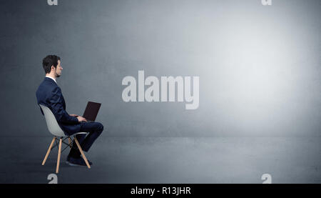 Businessman staying in an empty grey dark room with stuffs on his lap Businessman staying in an empty grey dark room with stuffs on his lap