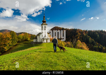 Man walking toward rural church in Slovenia with his dog. Stock Photo