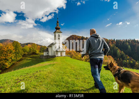 Man walking toward rural church in Slovenia with his dog. Stock Photo