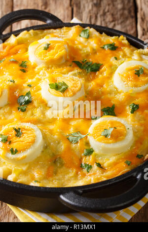 English Anglesey Egg baked mashed potatoes with leek sauce, cheese and boiled eggs close-up in a saucepan. Vertical Stock Photo