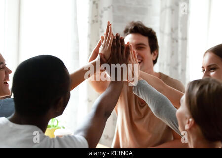 Diverse multiracial cheerful students giving high five greeting each other. Multi-ethnic millennial group of young people slapping palms sitting indoo Stock Photo