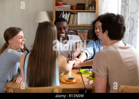 Group of millennial diverse students stacked putting holding hands together sitting around the table at university or college dormitory room. Friendsh Stock Photo