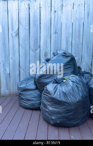 https://l450v.alamy.com/450v/r13n19/vertical-image-of-three-black-plastic-garbage-bags-packed-and-ready-to-take-out-sitting-on-the-deck-against-a-wooden-fence-r13n19.jpg