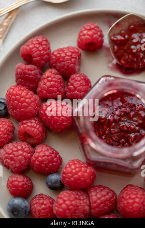 Raspberry jam in jar with berries near at gray plate Stock Photo