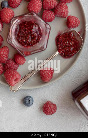 Raspberry jam in jar with spoon and berries near at gray plate Stock Photo