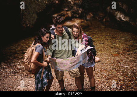 Man and two woman holding a navigation map while hiking. Tourists using a map to find the route to their destination. Stock Photo