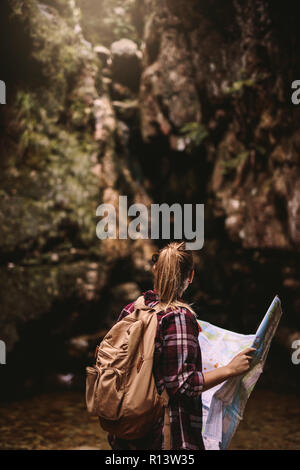 Rear view of young woman with backpack holding a route map looking at a view. Female hiker with map looking away. Stock Photo