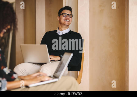 Smiling businessman in eyeglasses working on laptop looking away. Entrepreneurs working on their laptops sitting on chairs in office. Stock Photo