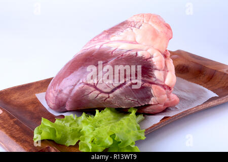 Raw beef heart and lettuce leaf on wooden desk isolated on white background from above and copy space. Stock Photo