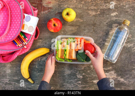 Sandwiches, fruits and vegetables in food box, backpack on old wooden background. Concept of child eating at school. Top view. Flat lay. Stock Photo