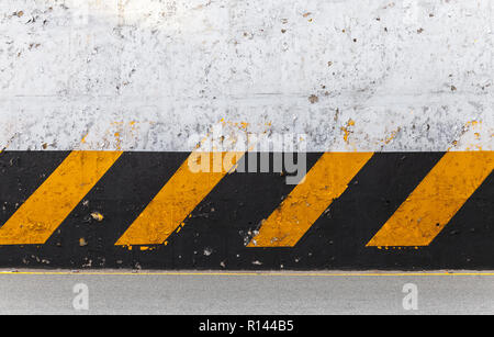 White concrete wall with striped yellow black caution pattern, urban roadside fencing Stock Photo
