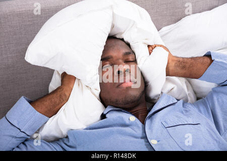 Man Covering His Ears With Pillow While Lying On Bed Stock Photo