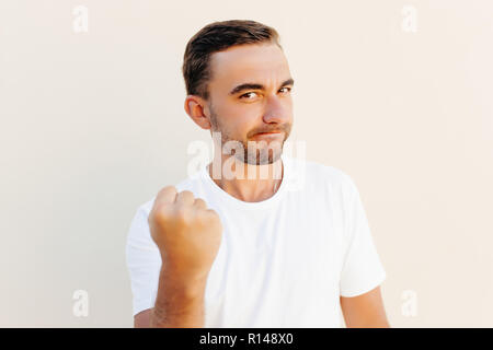 Closeup portrait, angry cranky upset young man, worker, business putting up fist about to give you knuckle sandwich, isolated orange background. Stock Photo