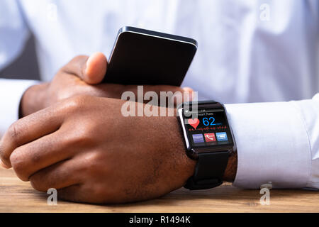 Close-up Of A Man's Hand Holding Mobile Phone With Smartwatch Showing Heart Rate Stock Photo