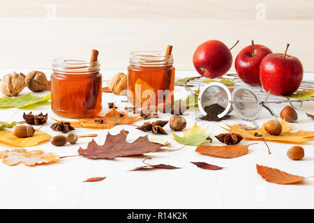 White wooden table with 2 glasses of tea with fall, autumn decoration and white background. Colorful leaves, lemon, cinnamon, walnuts, apples, tea, wa Stock Photo