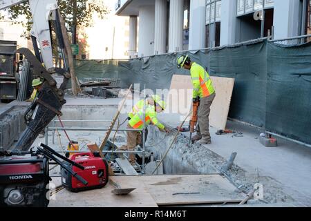 Three construction workers working on a sidewalk; jack hammer breaking concrete; excavation. Stock Photo