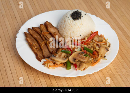 Dish of chinese cuisine on bamboo napkin. Pork with rice, mashrooms (?hampignon) and vegetables Stock Photo