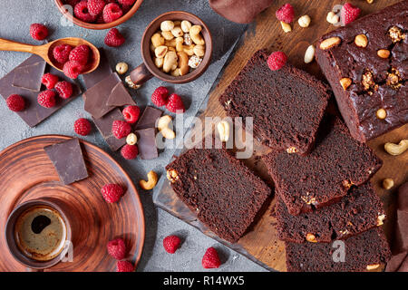 overhead view of chocolate  pound cake with nuts and raspberries cut in slices on a wooden board on a concrete table with cup of coffee and brown clot Stock Photo