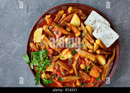 overhead view of okra tomatoes vegetables stew, served with feta cheese slices on a clay plate on a grey concrete table, greek recipe, view from above Stock Photo