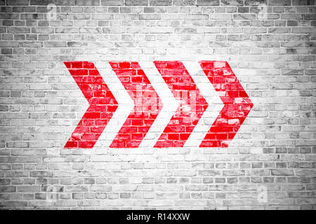 Red directional arrow signs pointing direction painted on a white gray brick wall signboard texture background. Stock Photo