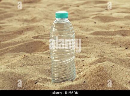 Bottle with sparkling crystal drinking water with a red lid on the sand on a background of the beach on a hot sunny afternoon closeup. Stock Photo