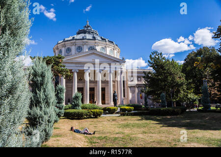 Bucharest, Romania - September 25, 2018 - a woman relaxes in the sun on the grass in front of Roman Athenaeum, Bucharest's most prestigious concert ha Stock Photo