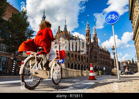 AMSTERDAM, THE NETHERLANDS - September 7, 2018: a woman cycles on Amsterdam street under blue cycle path sign; Magna Plaza shopping mall in the backgr Stock Photo