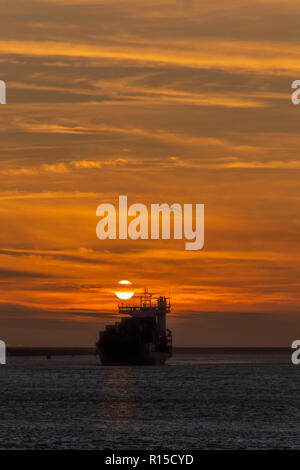 Container vessel leaving the Rotterdam seaport toward the deep ocean under a vivid sunset, Amsterdam, Netherlands Stock Photo