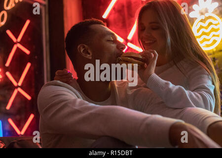 Young woman feeds a man a burger. Couple having fun. Stock Photo
