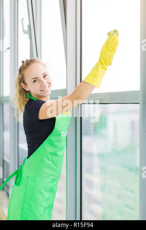 Smiling young woman worker cleaning soap suds on glass window with squeegee and rag Stock Photo