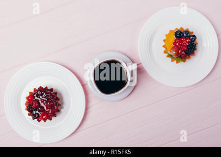 Composition of delicious small cakes with espresso on pink wooden table, top view. Flat lay arrangement of black coffee and berry tartlets. Stock Photo