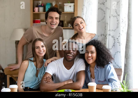 Happy multiracial people millennial girls guys sitting at desk smiling looking at camera, people spending time together are best friends. Friendship b Stock Photo